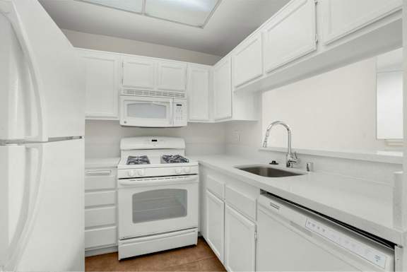 A white kitchen with a refrigerator, microwave, oven, and sink.