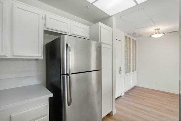 A stainless steel refrigerator is in a kitchen with white cabinets.