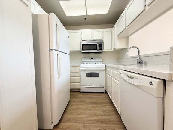 A kitchen with white appliances and wooden floors.