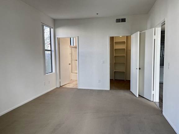 A large empty room with a door on the left and a shelving unit on the right.