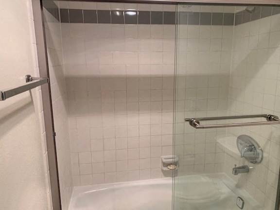 A white tiled shower with a glass door and a silver grab bar.