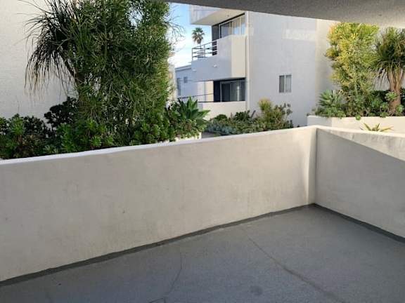 A balcony with a concrete floor and a white wall with a building in the background.
