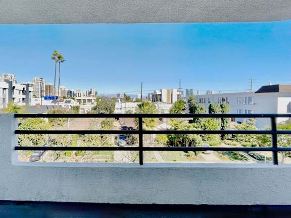 A balcony overlooks a residential area with houses and palm trees.