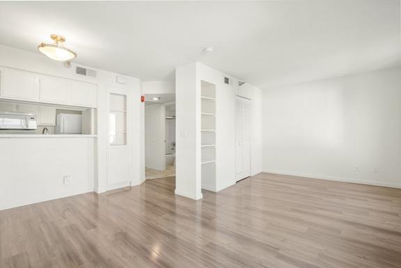 A white room with a wooden floor and a kitchen area to the left.