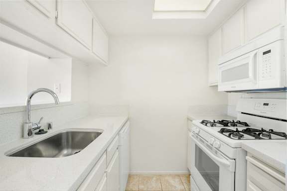 A white kitchen with a stove, sink, and microwave.