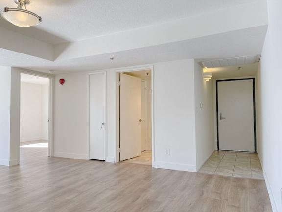 A room with white walls and wooden flooring with three doors.