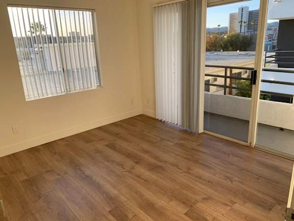 A room with wooden flooring and a view of the outside through a sliding glass door.