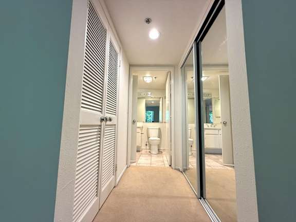 A hallway with a toilet and sink visible through the mirror.