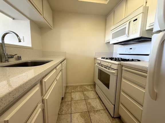 A kitchen with white appliances and a tiled floor.