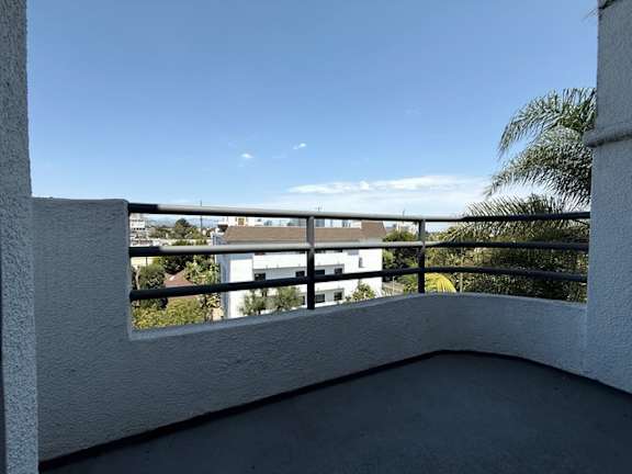 A balcony with a white wall and a black railing overlooking a building and trees.