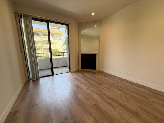 A room with wooden flooring and a large window with a view of a building outside.