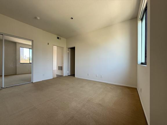 A large empty room with a carpeted floor and a window.