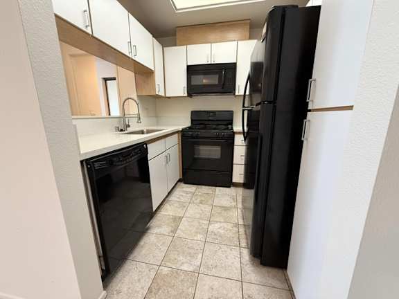 A black refrigerator stands in a kitchen with white appliances and cabinets.