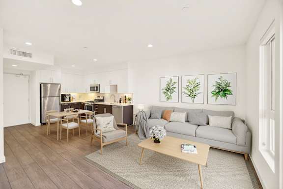 A modern living room with a grey sofa, wooden coffee table, and a kitchen area in the background.
