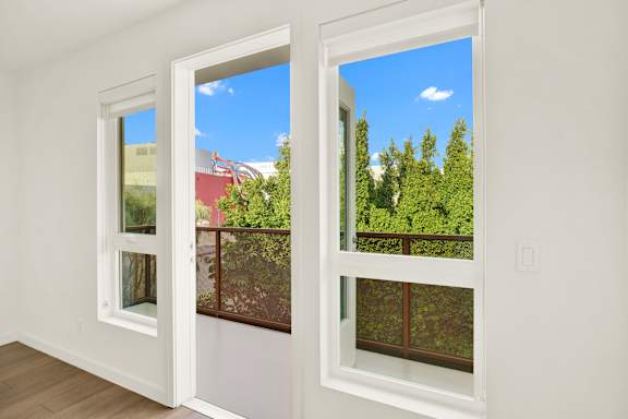 A room with two windows overlooking a red building and green trees at The Urbanpolitan, Los Angeles