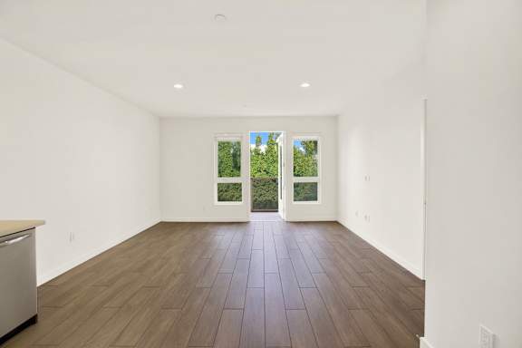 A large empty room with a dishwasher on the left and a window with a view of trees outside at The Urbanpolitan, Los Angeles, California