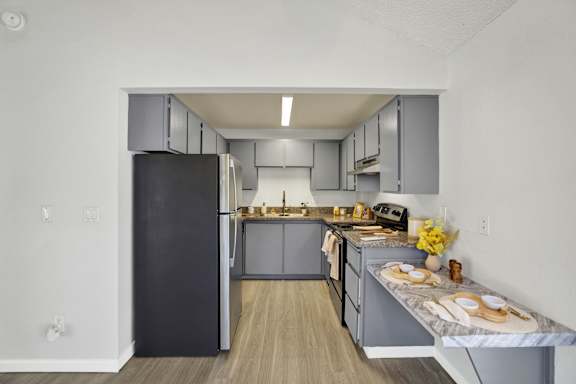 A kitchen with a black refrigerator and wooden floors.