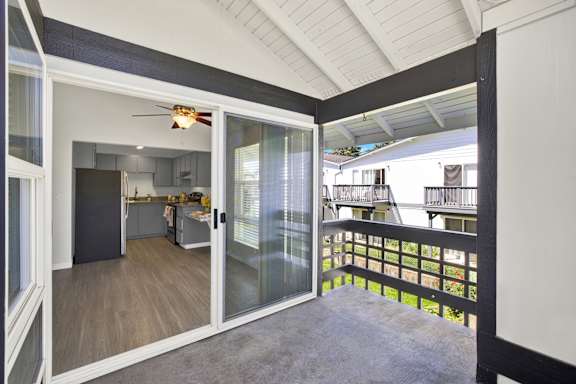 A balcony with a glass railing and sliding glass doors leading to a kitchen.
