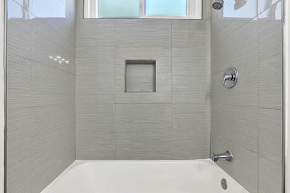 A white bathtub in a bathroom with grey tiles.at Federal Apartments, Los Angeles, 90025