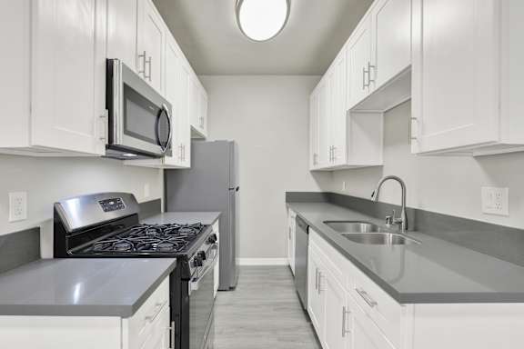 A kitchen with white cabinets and a black stove top oven.at Barton Apartments, California