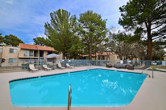 A swimming pool surrounded by trees and chairs.