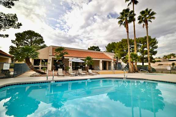A swimming pool in front of a building with palm trees.