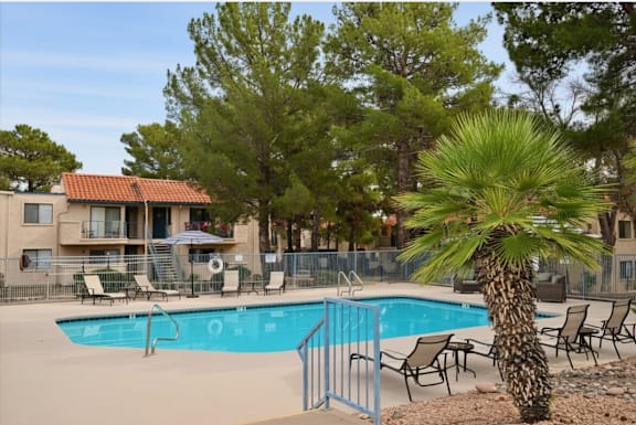 A pool surrounded by chairs and trees with a building behind it.
