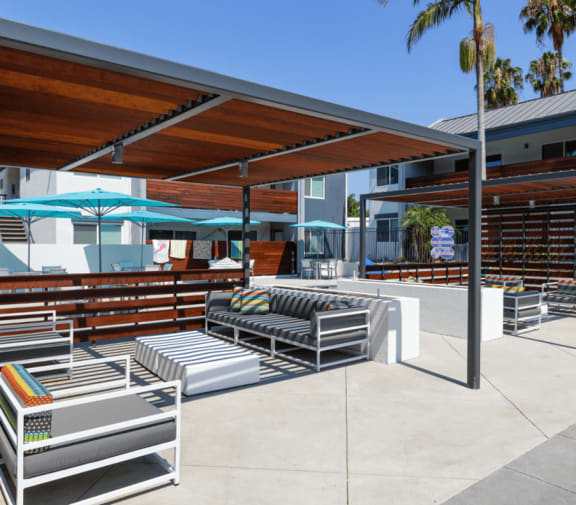 an outdoor lounge area with lounge chairs and umbrellas with palm trees in the background at Beverly Plaza Apartments, California, 90815