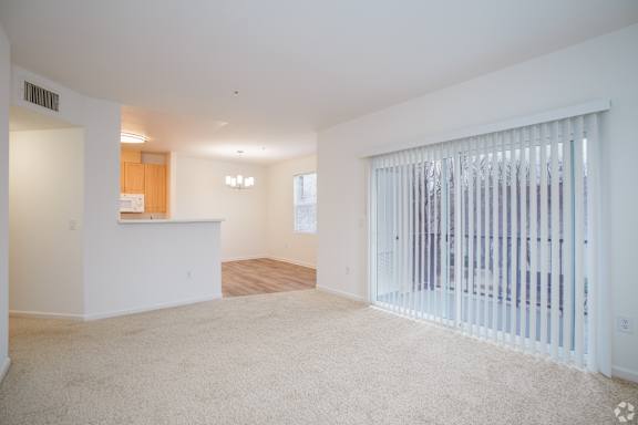 A spacious living room with a white carpet and a sliding glass door.