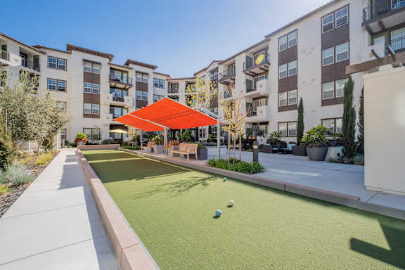 an outdoor bocce court with an orange awning in front of an apartment building at Deer Creek Apartments, San Ramon, CA