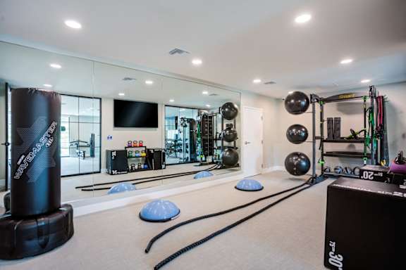 A gym with a variety of equipment including a weight bench, a rowing machine, and a television at Pradera Apartments, San Ramon, California