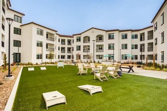 A grassy courtyard with chairs and tables in front of apartment buildings at Pradera Apartments, San Ramon, 94582