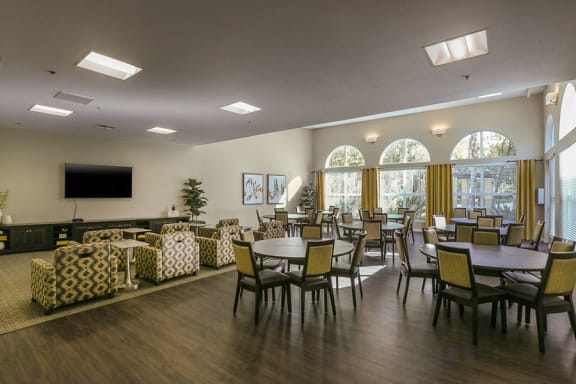 a large room with tables and chairs and a television on the wall  at Tesoro Senior Apartments, Porter Ranch, CA, 91326