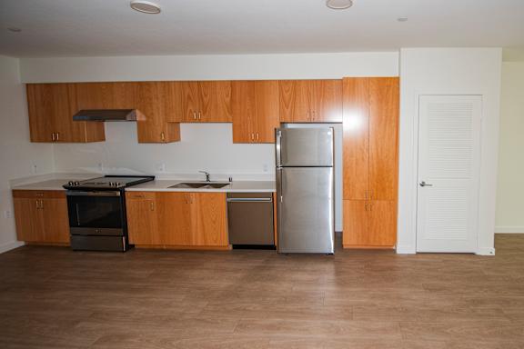 A kitchen with wooden cabinets, white countertop and a stainless steel refrigerator, dishwasher, and stove.
