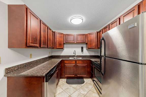 A kitchen with a refrigerator, sink, and cabinets.