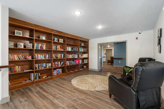a library with a black leather chair and a book shelf at 41 North Senior Living Apartments, Fort Wayne, IN