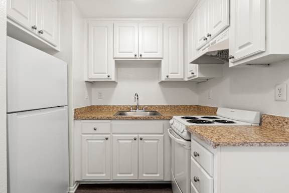 A white kitchen with granite countertops and white appliances.