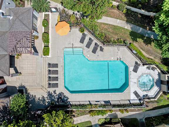An aerial view of a swimming pool surrounded by a concrete patio and a small fountain.
