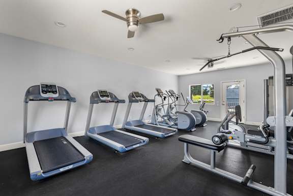 A gym with treadmills, elliptical machines, and a fan.