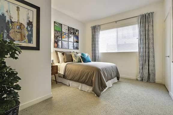 A bedroom with a bed, a guitar picture, a window with curtains, and a carpet.at Vues on Gordon, Los Angeles, 90028