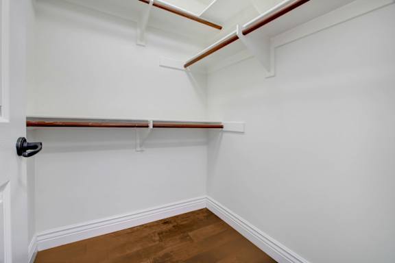a walk in closet with white walls and a wood floor