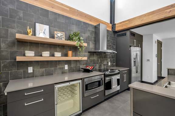 A modern kitchen with a grey tiled backsplash and wooden shelves.