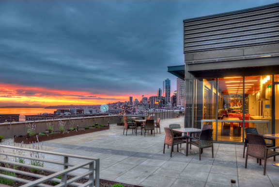 A patio with chairs and a table overlooking a city skyline at sunset.