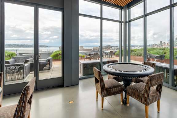 A round table with chairs is set up in a room with a view of the city.
