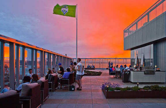 people sitting at tables on a roof terrace at sunset