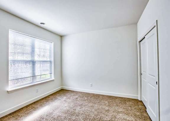 A room with a carpeted floor, a window with blinds, and a white door.