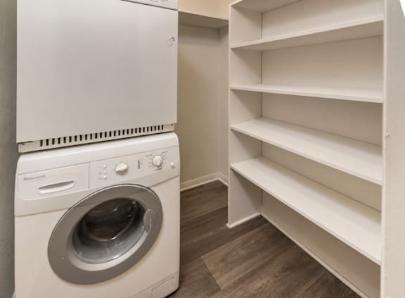 A white dryer and washer in a small laundry room with shelves.