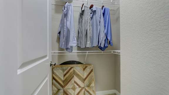 A closet with clothes hanging and a wicker basket on the shelf.