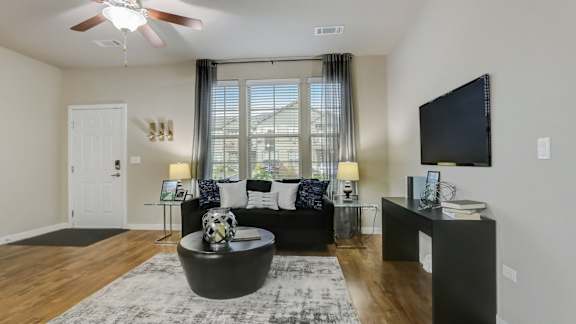 A living room with a black couch, a television, and a ceiling fan.