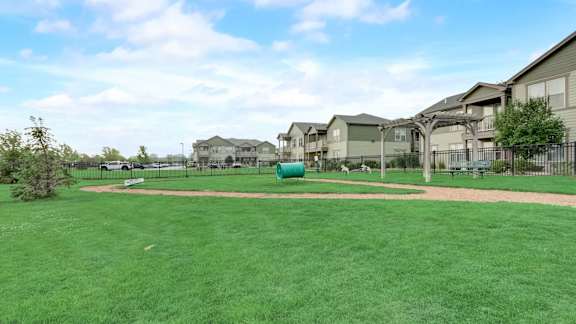 A grassy field with a playground and apartment buildings in the background.